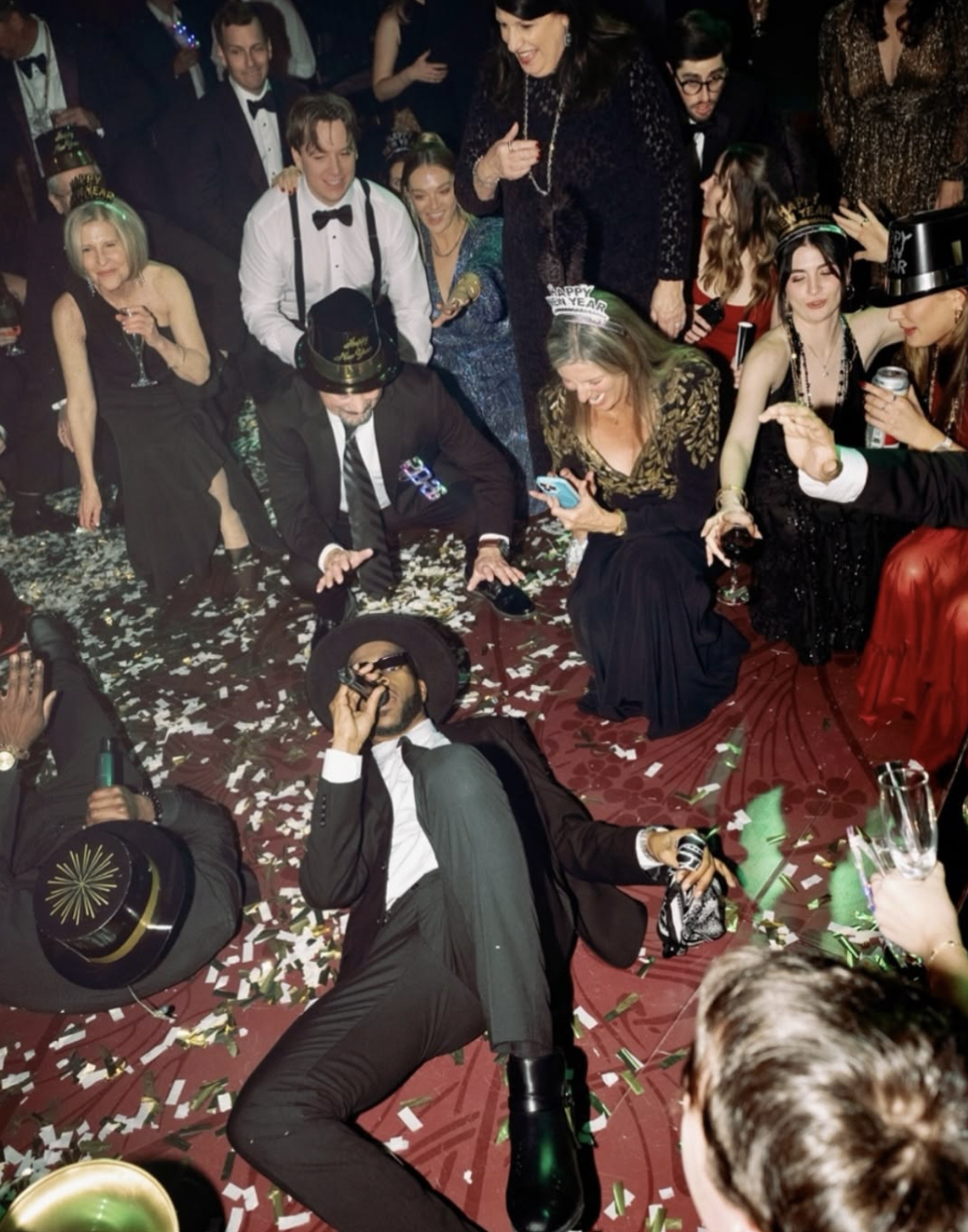 A man in a suit, trilby hat and sunglasses lays singing on a floor with an enthusiastic crowd all around him.
