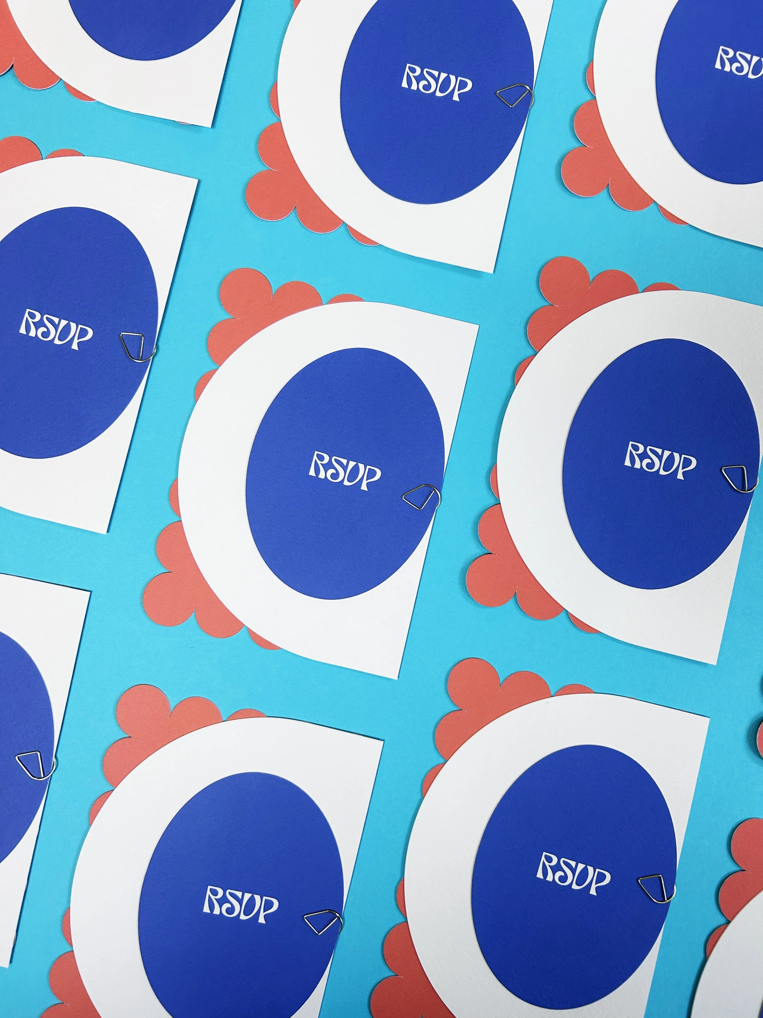 Invitation packs which include a stack of cards in different colours and shapes, held together with a gold paperclip.