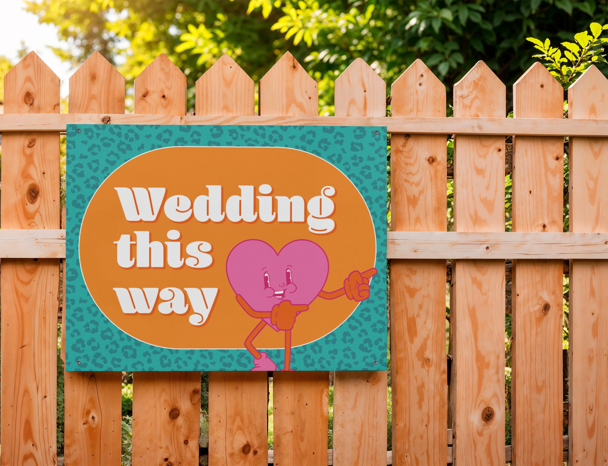 A sign mounted on a fence with the words 'Wedding this way' and a cartoon heart with a smily face pointing to the left.