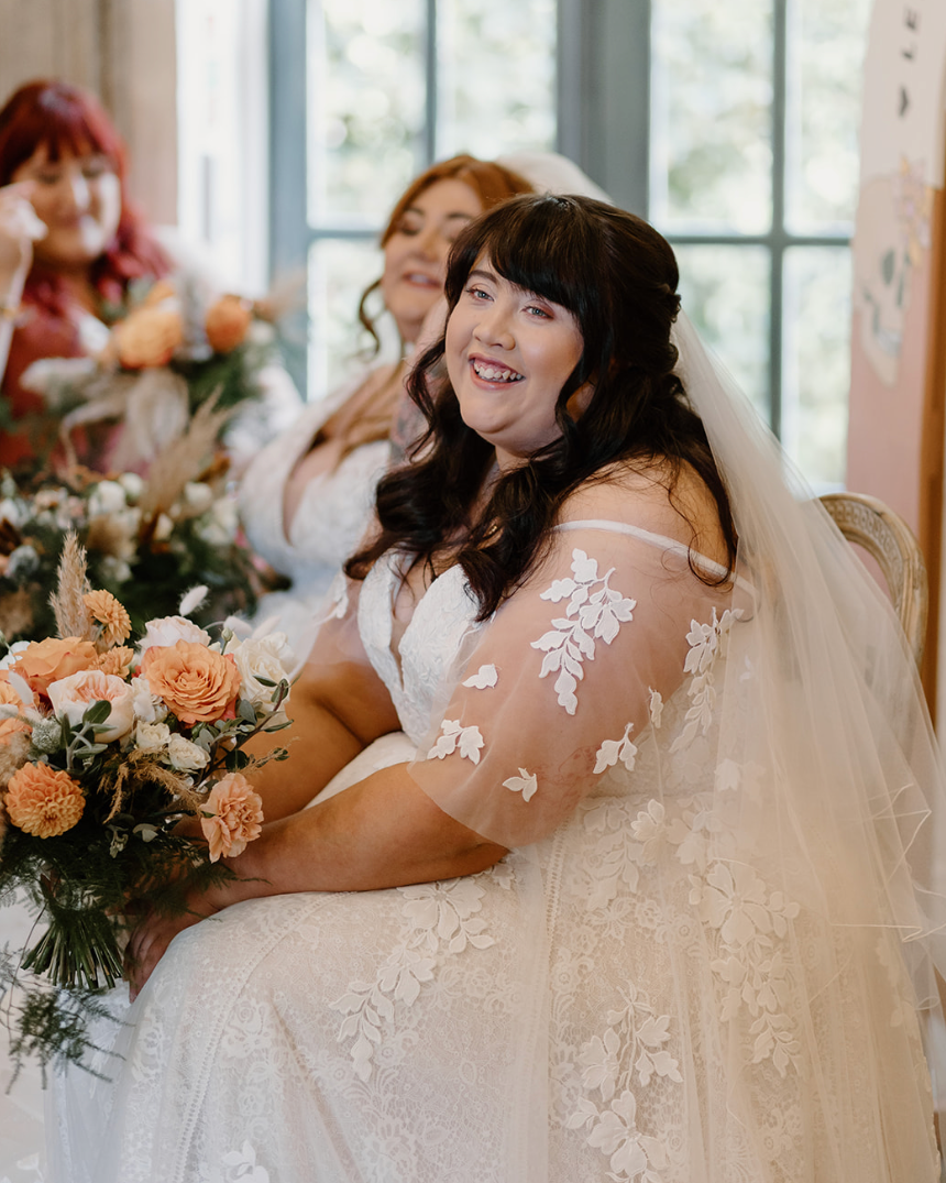 A bride with long brown hair smiles just past the camera.