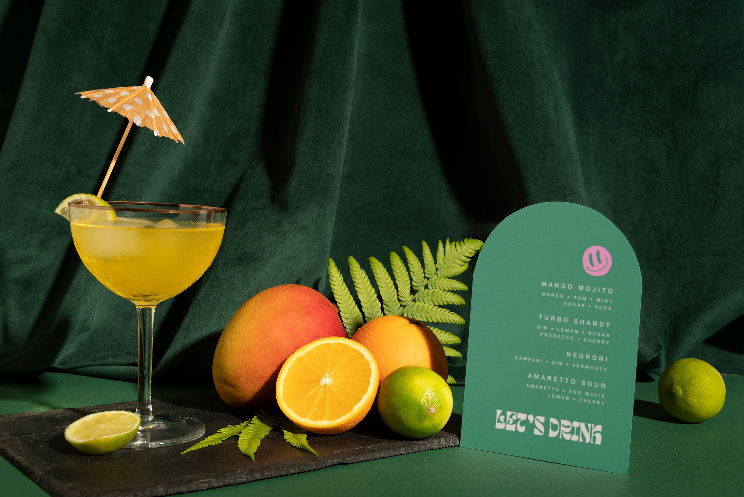 Fruit and a cocktail glass next to an arched cocktail menu sign.