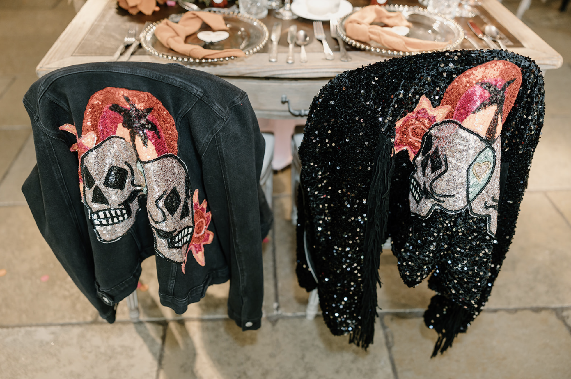A leather jacket and a sequin jacket hang on the back of two chairs, both adorned with a custom skull motif.