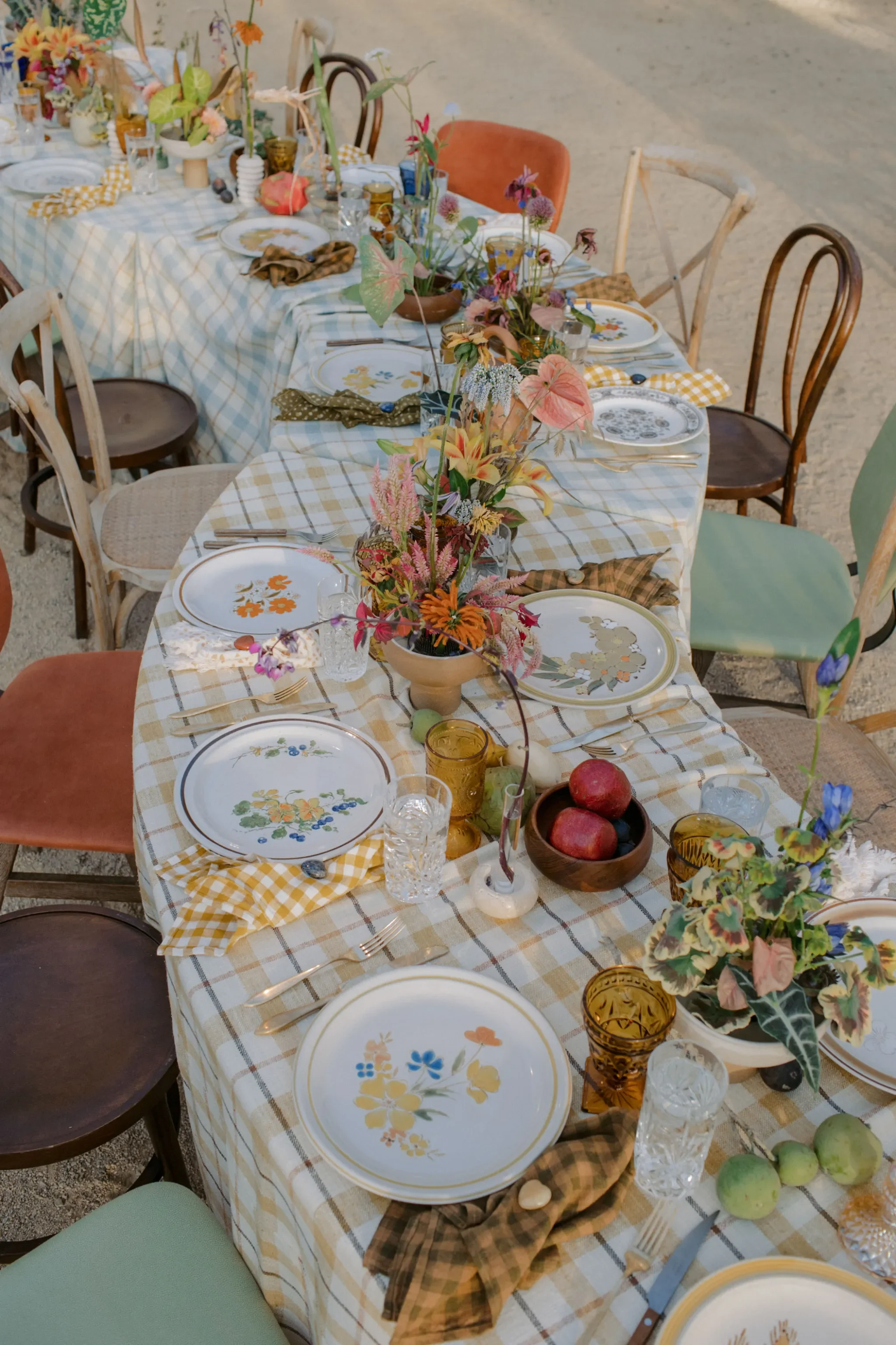 A tablescape with vintage glassware and crockery and mismatching chairs, shot from above.