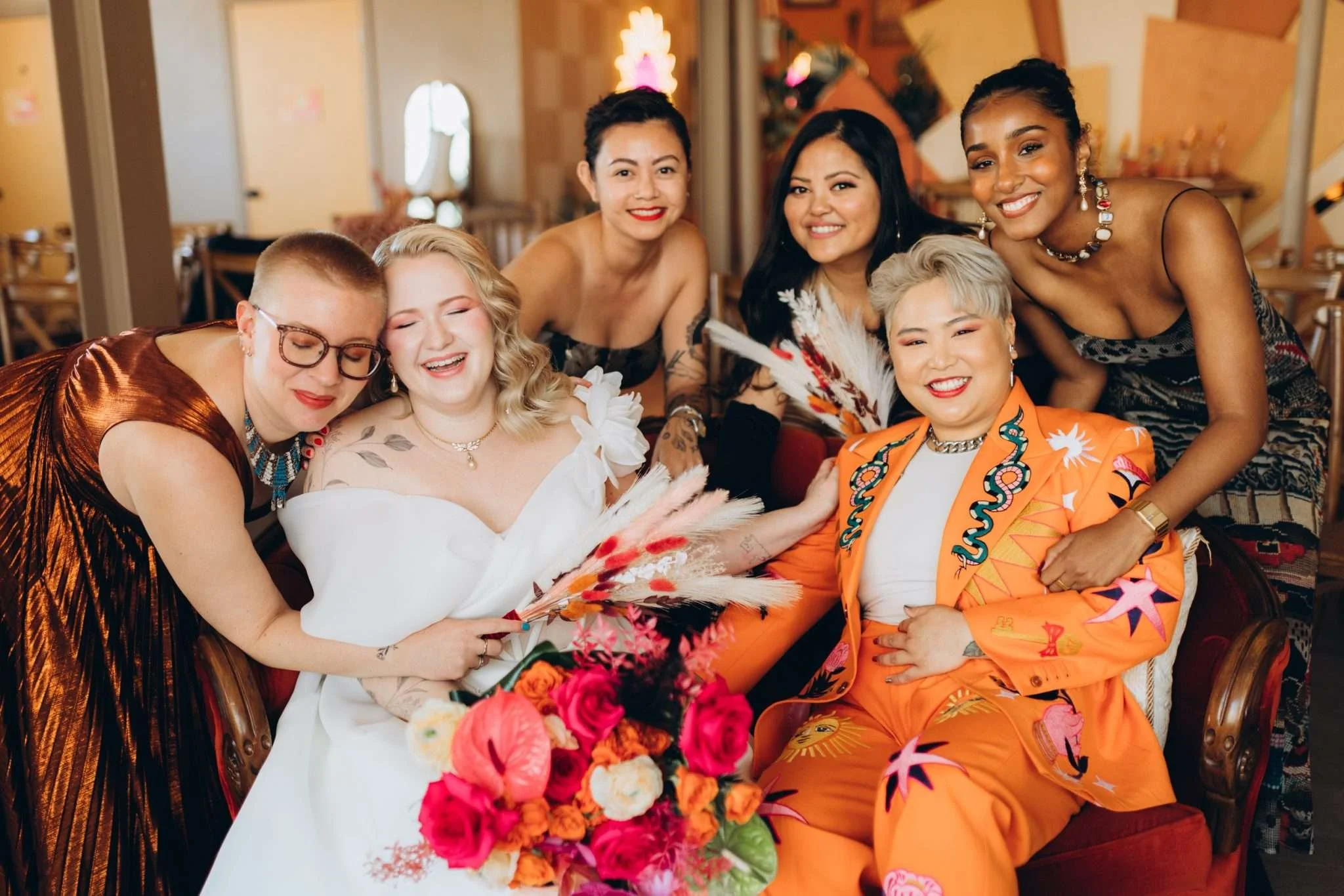 Two newlyweds sit with their loved ones stoof behind, and everyone is smiling.