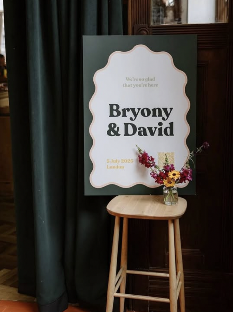 A welcome sign rests on a stool alongside a small vase of pretty flowers.