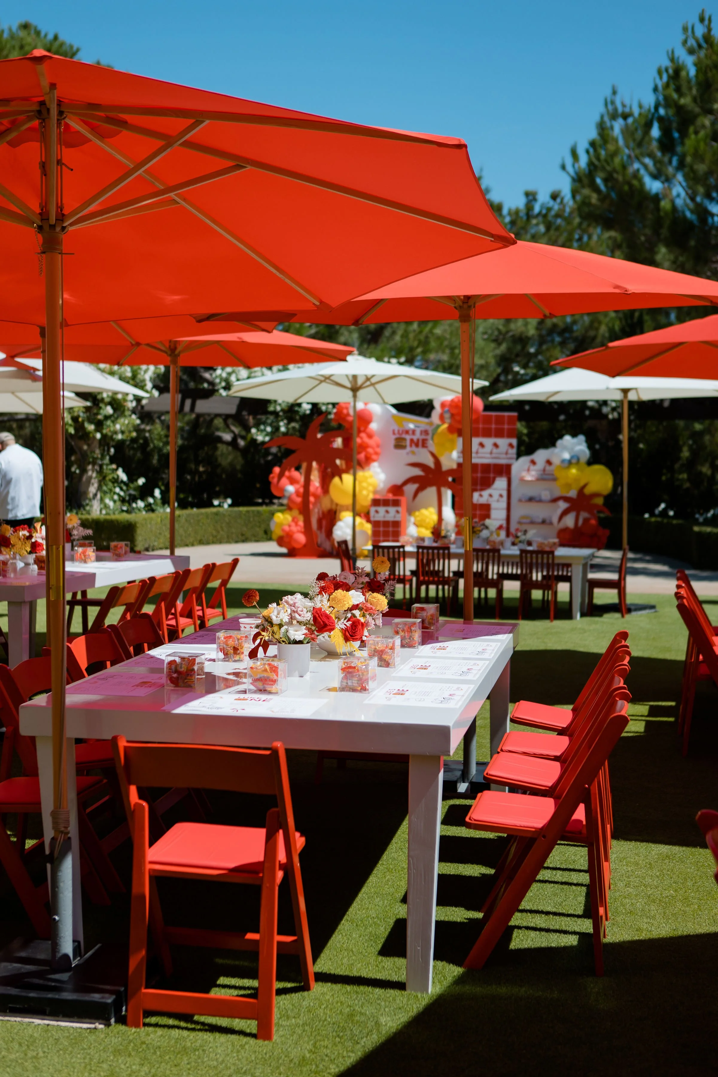 Outdoor first birthday party setup with color coordinated theme, floral centerpieces, and colorful coordinated signage and decorations.