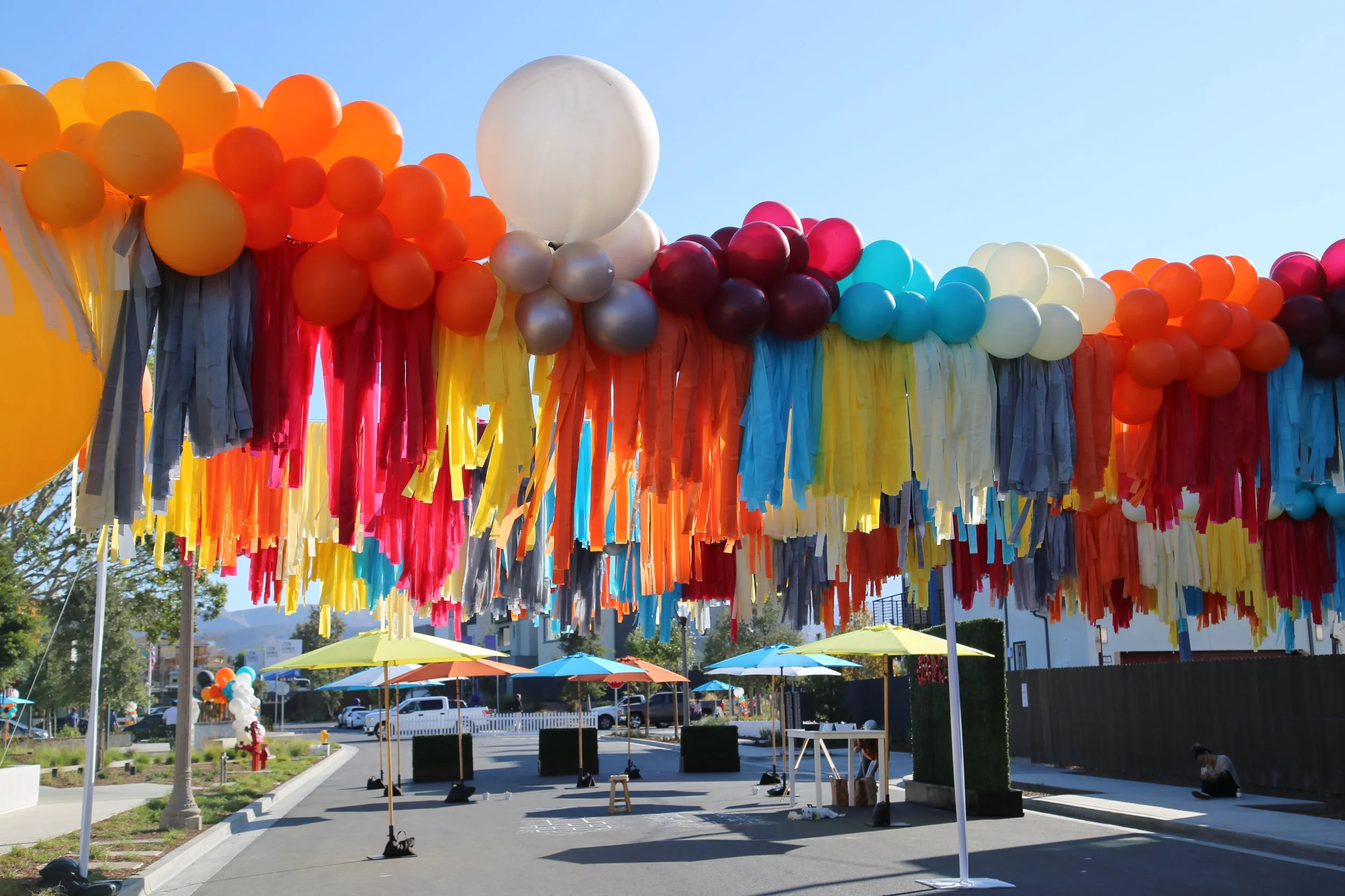 Model Grand Opening in Irvine, vibrant outdoor celebration featuring colorful balloon decorations and fabric draping in a festive event setting. 