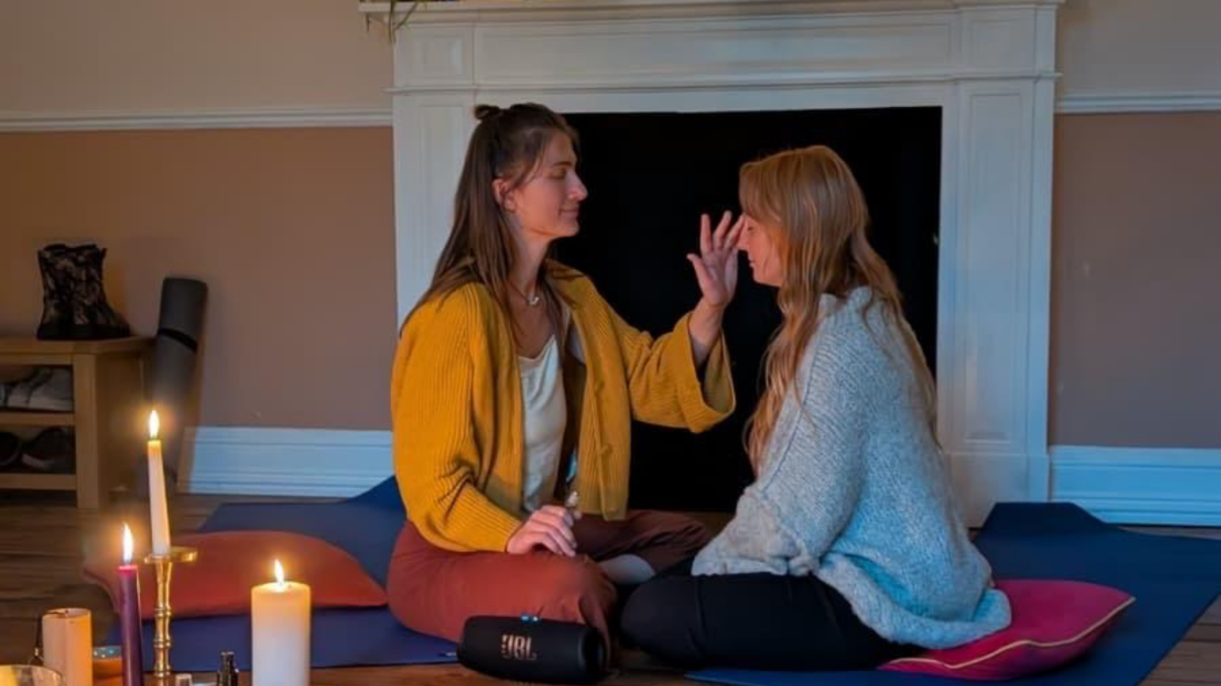 two women sat in front of an altar facing each other anointing one another
