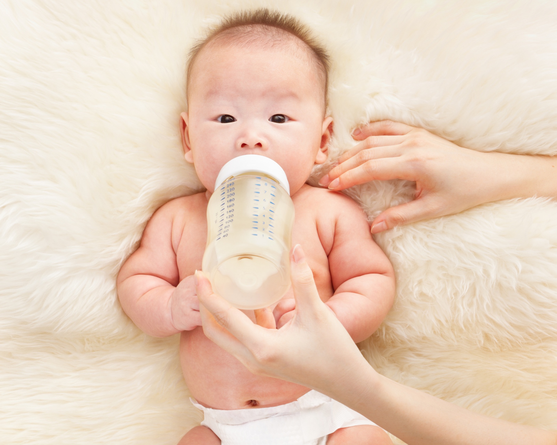 Image Of a Baby drinking bottle of pumped breast milk naked in a diaper with big rolls.