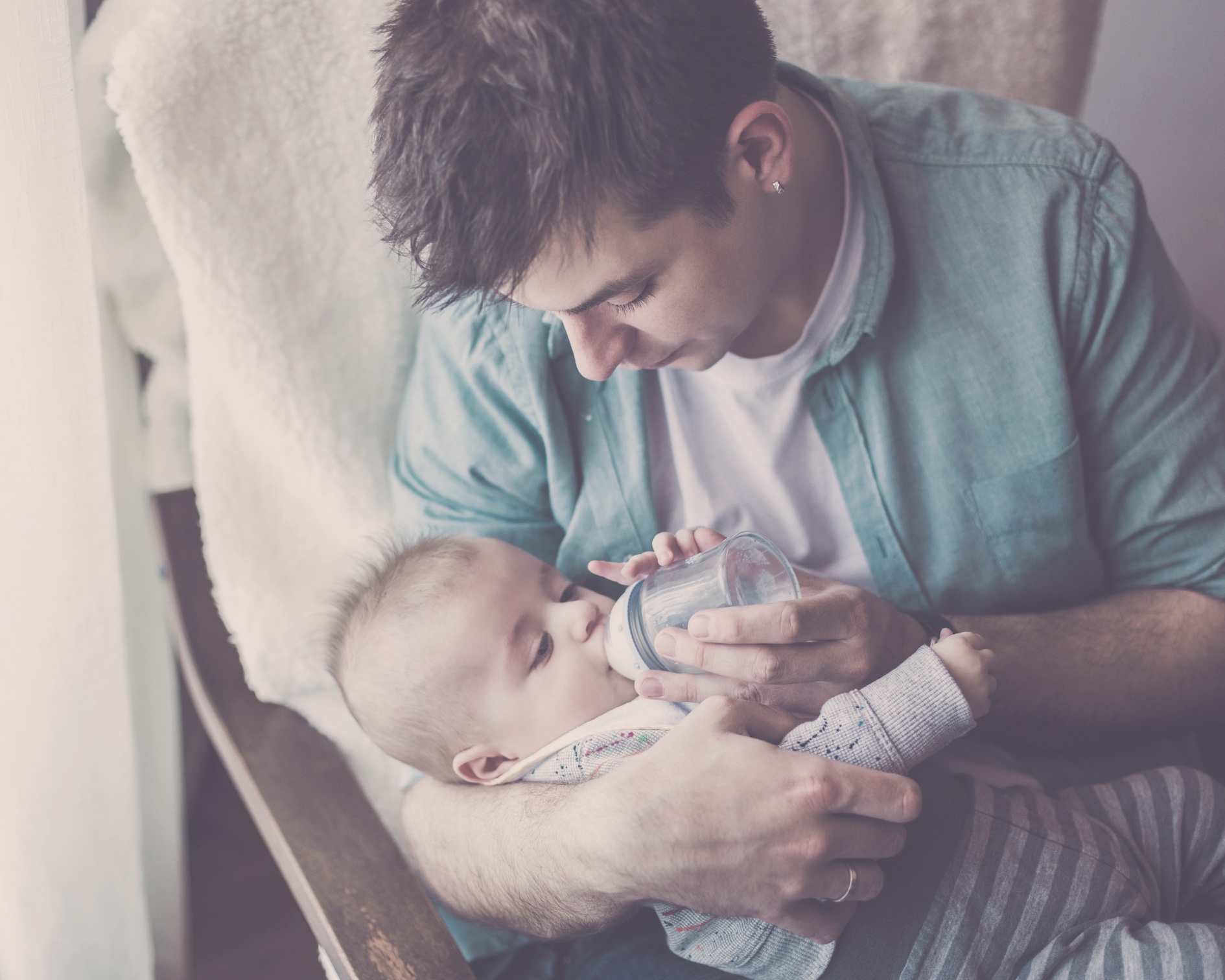 Image of caregiver feeding baby a bottle while rocking baby in quiet room.