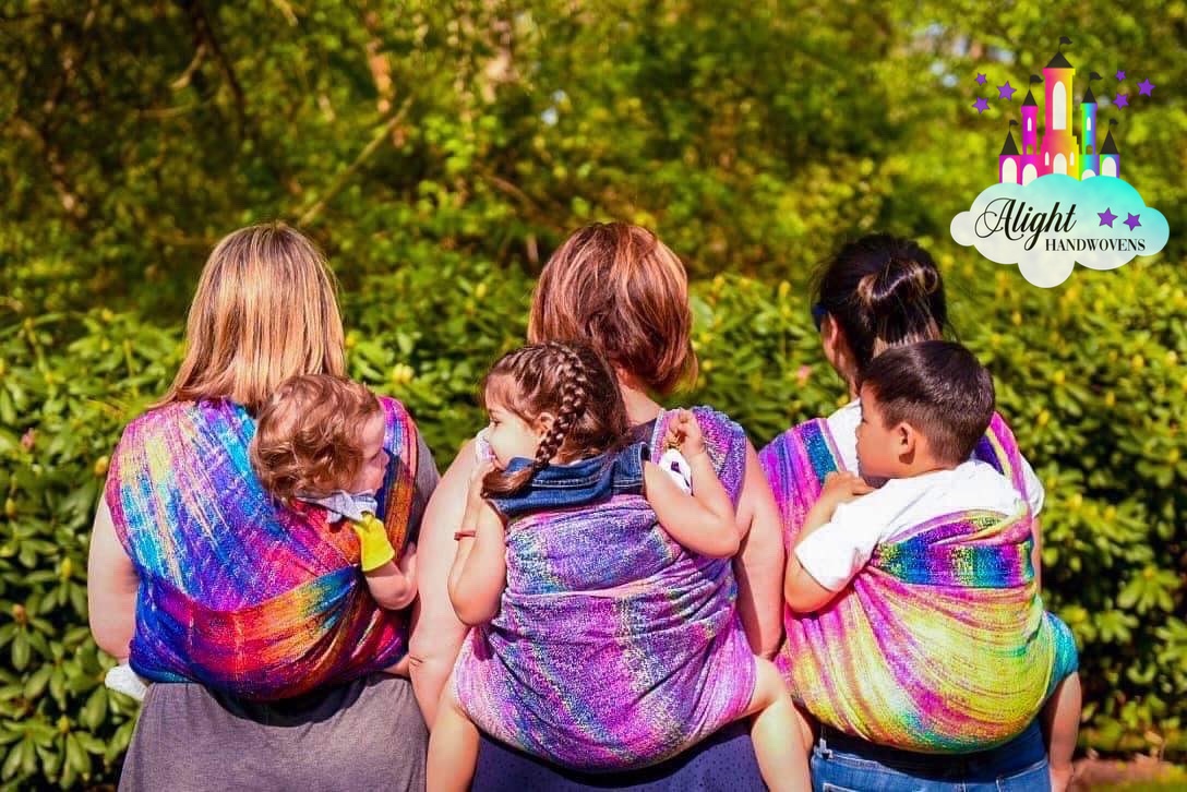 Photo of Three Women All wearing their babies on their backs. Alight Wraps From left to right: East Gate, Cair Paravel, and Moonlit Pandora.