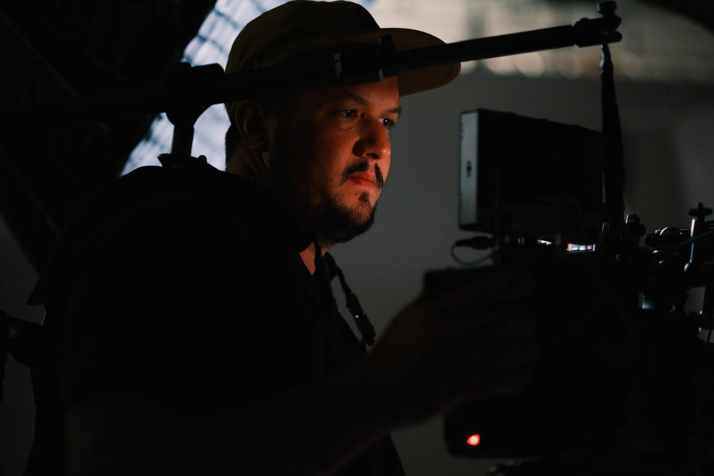 A man with a hat operating a professional camera in a dark environment, focused on filming or photography.