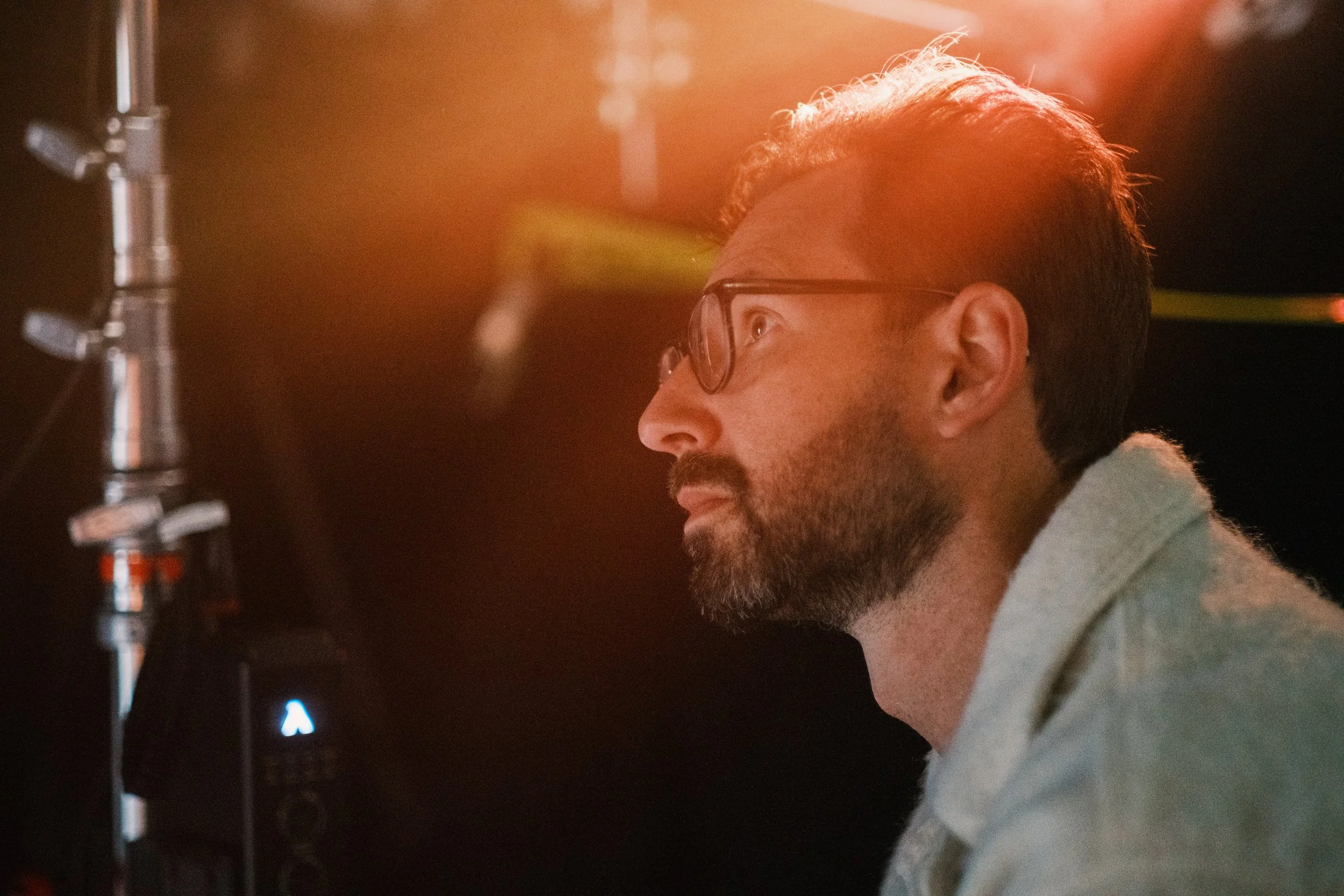 Filip Cerovic, aka Phil Cera, is a Branded entertainment director and showrunner creating scripted/unscripted films and campaigns. Side profile of a man with glasses and a beard working with audio or recording equipment, illuminated by warm lighting.