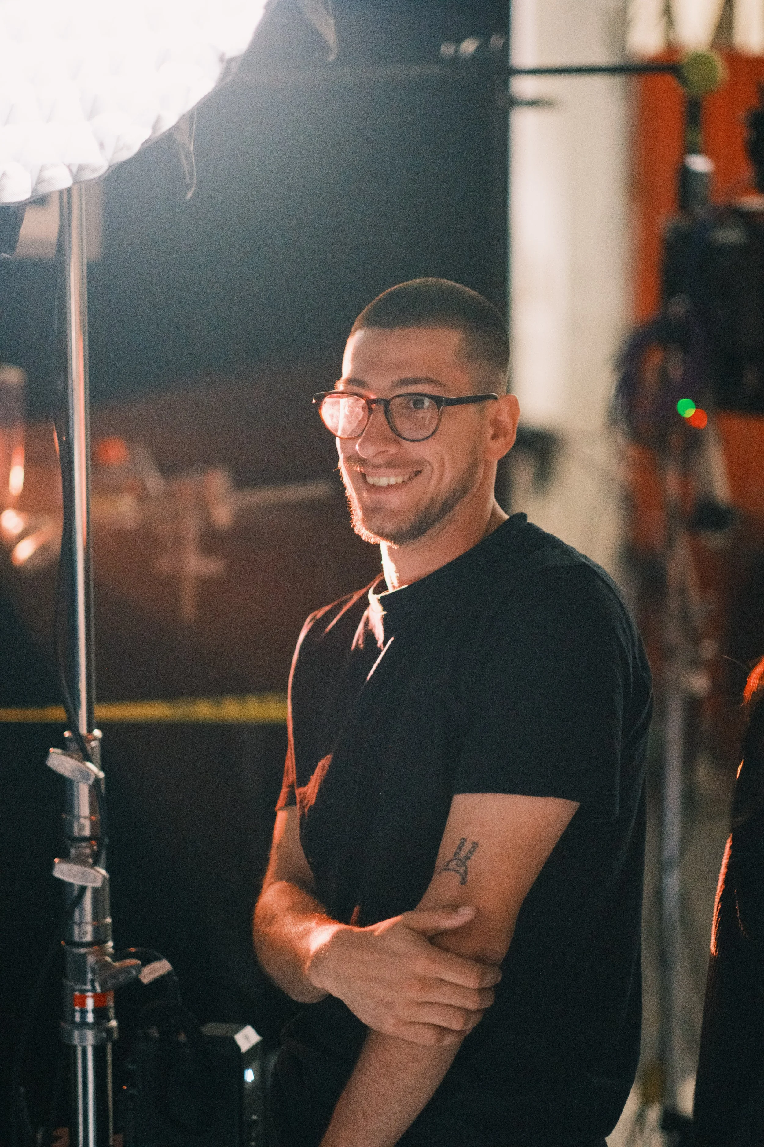 A smiling man wearing glasses and a black t-shirt standing in a photography or film studio.