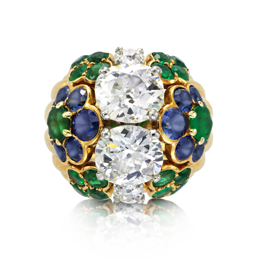 A Cartier diamond cocktail ring is the consummate gift for the glamazon. Designed with two old-mine cut cushion diamonds within calibre-cut emerald and sapphire circular flowerheads mounted in gold 1960's. Weight of diamonds approximately 1.95 carats and 2.13 carats respectively.