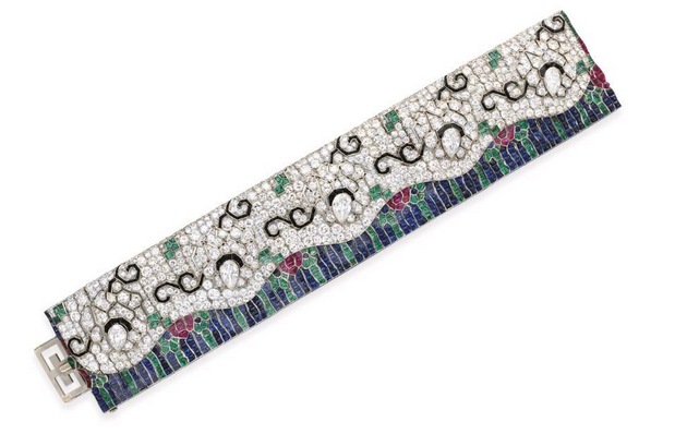 An Art Deco diamond and multi-gem "Wave" bracelet, by Rubel Frères The wide articulated band designed as an old European and circular-cut diamond undulating upper panel, set with five pierced flowers each bezel-set with a pear-shaped diamond pistil and calibré-cut black onyx stems and detail, enhanced by buff-top emerald accents, framed by calibré-cut emeralds, rubies and sapphires depicting a floral scene, mounted in platinum, circa 1925, 7½ ins., with French assay marks With maker's mark for Rubel Frères