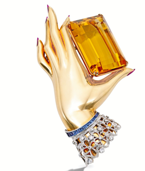 Flato was especially attracted to hand imagery, which was a frequent theme in his pieces. A Gold, Platinum, Citrine, Ruby, Diamond and Sapphire Clip-Brooch, by Paul Flato The polished gold hand with five drop-shaped cabochon ruby fingernails holding an emerald-cut citrine weighing approximately 100.00 carats, the lace cuff set with round and single-cut diamonds weighing approximately .50 carat, accented by 15 calibré-cut sapphires; circa 1940.