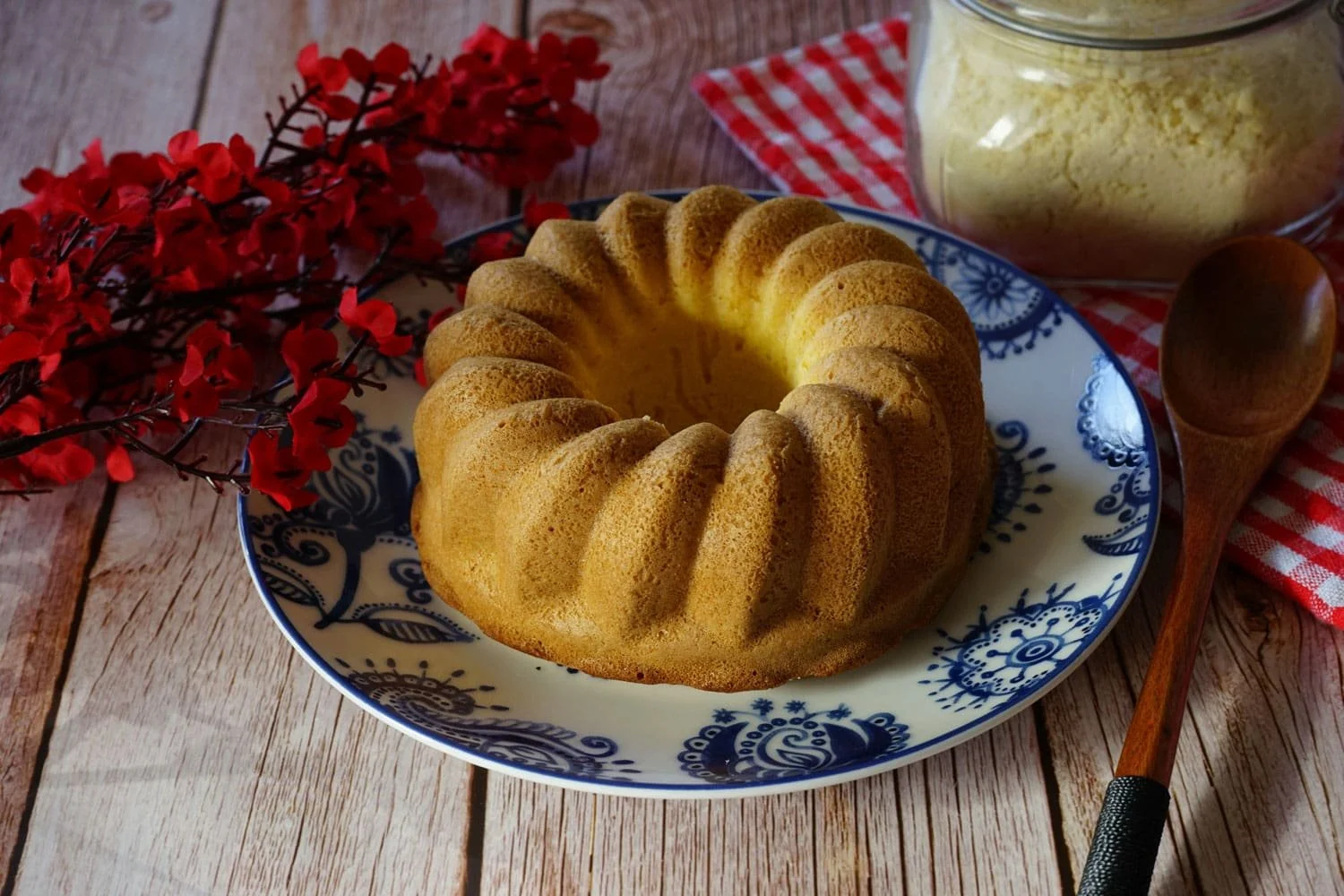 Ring-shaped Italian cake served on a blue and white ceramic plate beside red flowers and a wooden spoon. Traditional desserts and local cuisine are part of the culinary things to do in Ravello.