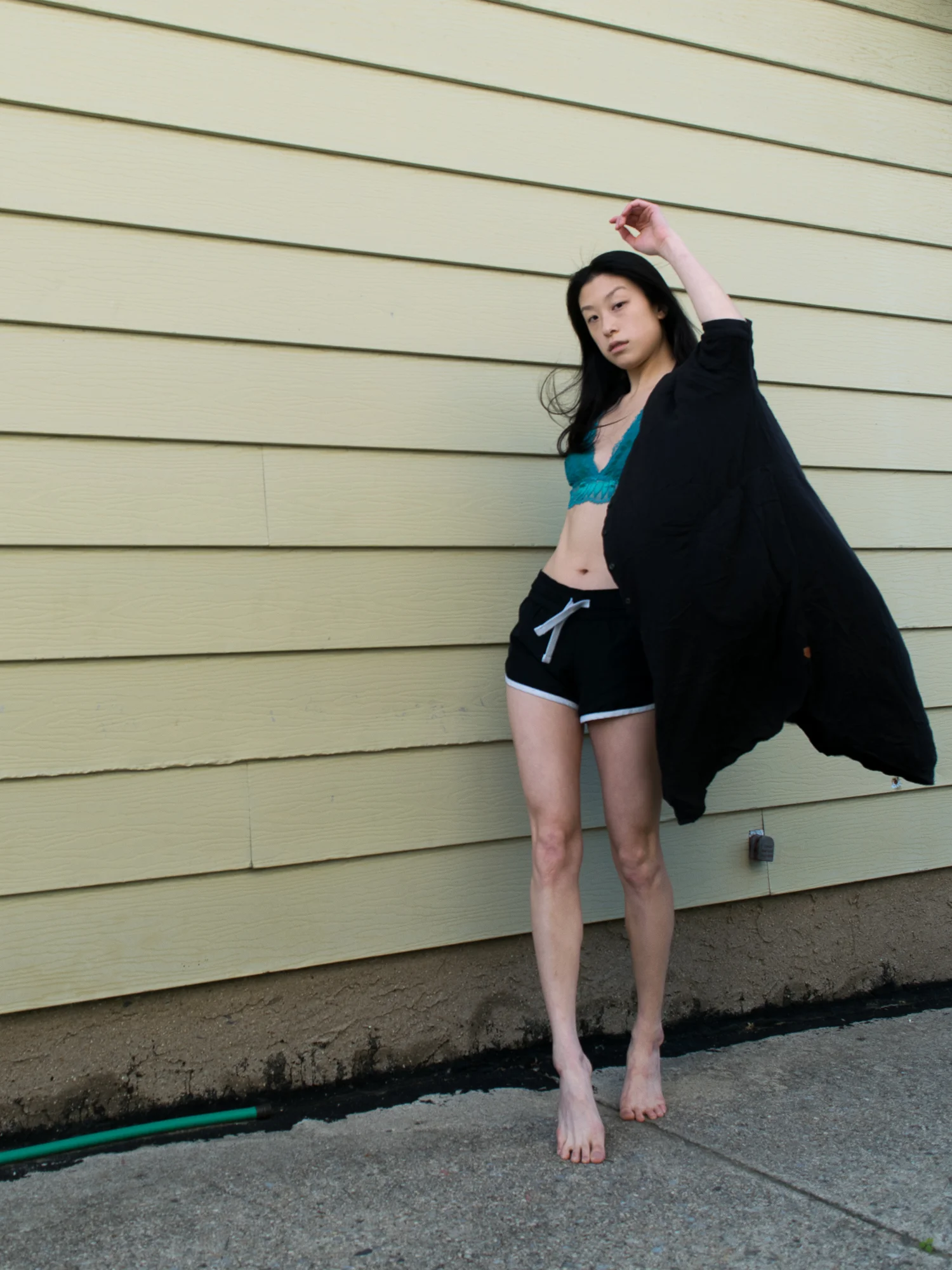 Female East asian blogger in black athletic shorts and blue bralette top with black shirt-dress cover-up