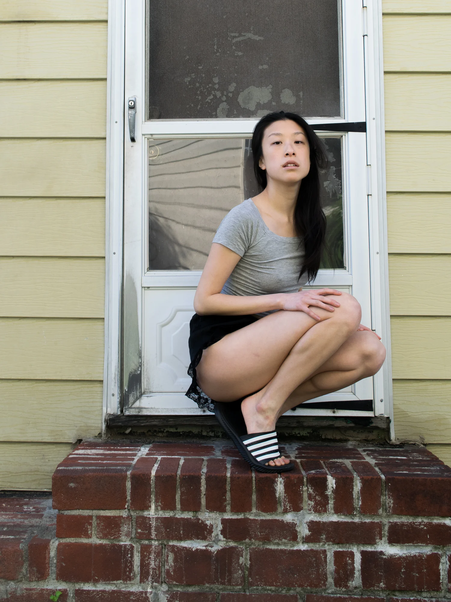 Female, east asian blogger in grey cropped t-shirt, lacy black shorts, black and white striped sandals, posing on brick stoop