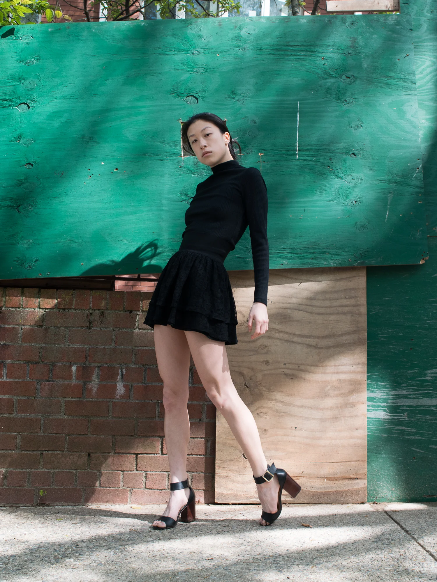 Female east asian style blogger wearing all-black outfit with cropped turtleneck top, short flared shirt, and heeled sandals