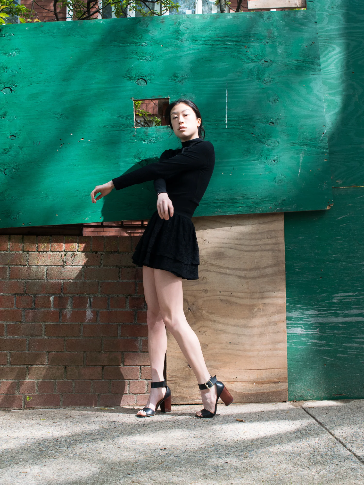 East asian female style blogger in all-black kpop inspired summer outfit against green and brick wall