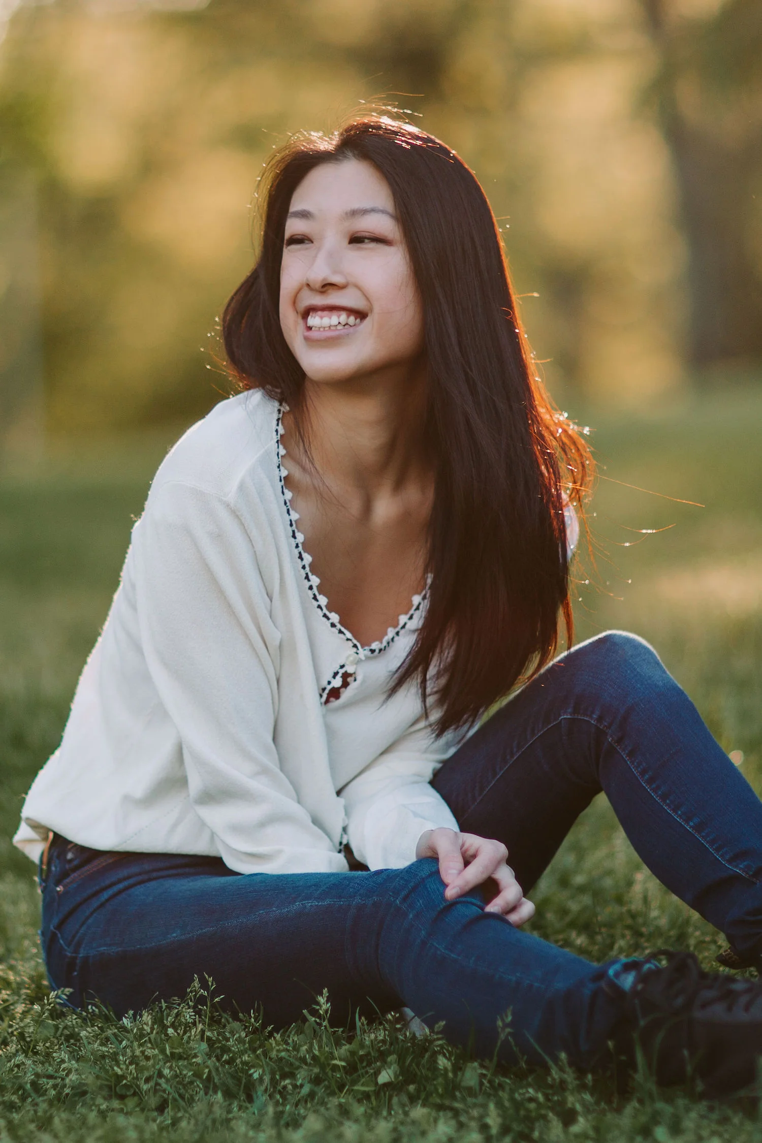 Photo of style blogger, Gi Shieh wearing white cardigan and blue jeans sitting in Central Park grass at golden hour
