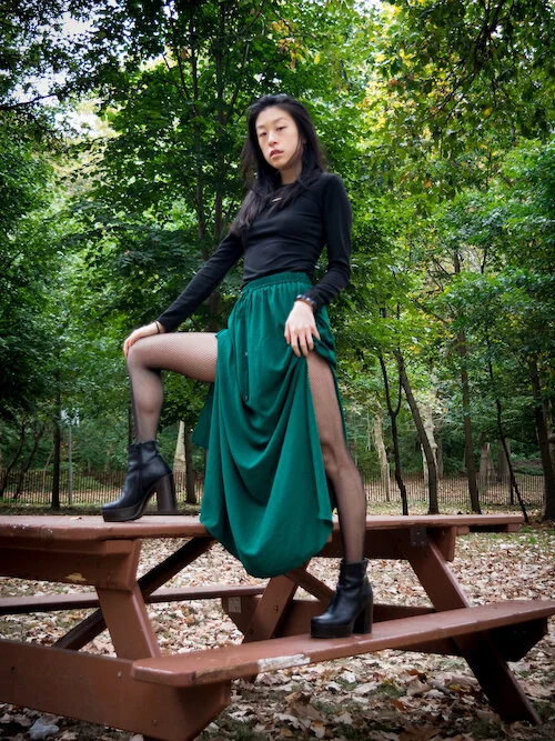 Sustainable style blogger wearing black dress, green skirt, black boots, fishnet tights