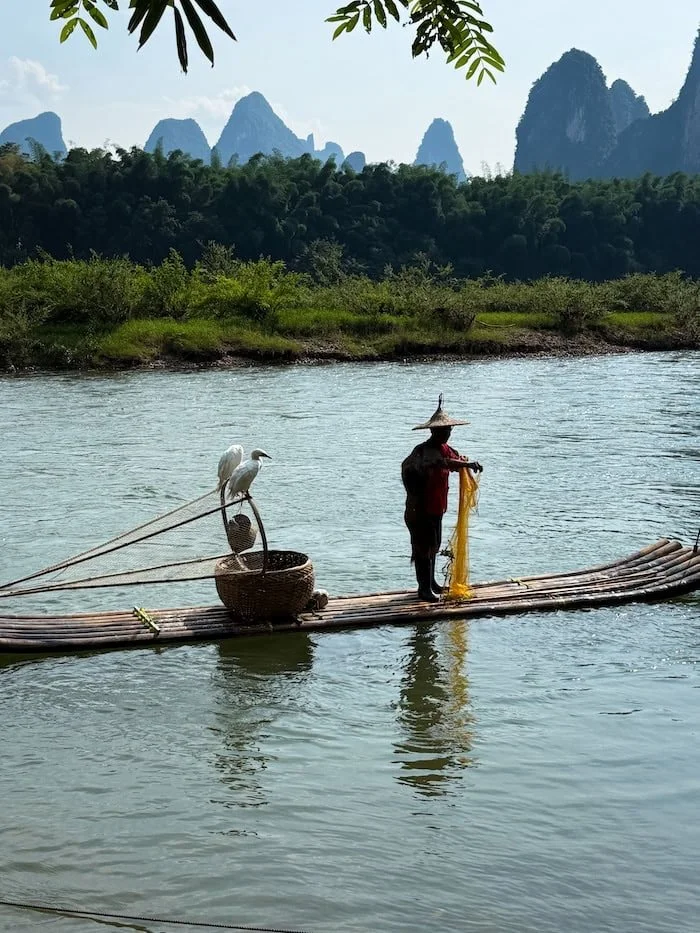 A cormorant fisherman preparing his net on a bamboo raft along the Li River.