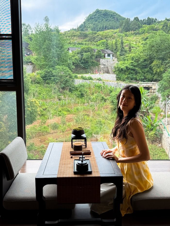 Traveler enjoying tea by a large window with views of the surrounding countryside. 