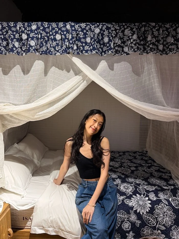 Traveler sitting on a canopy bed inside a cozy boutique room in a traditional village.