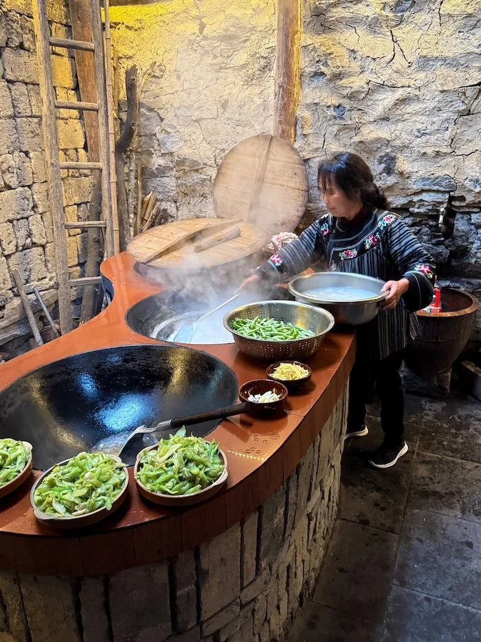 Local cook preparing fresh vegetables and traditional dishes in a rustic village kitchen.