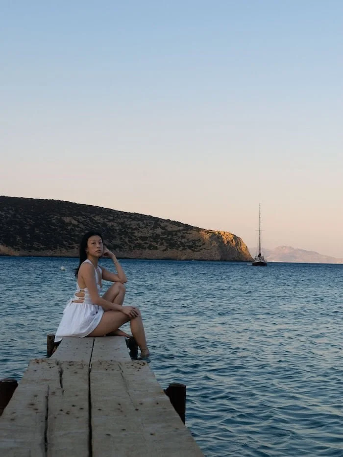  Woman sitting on a wooden dock overlooking the Aegean Sea. The best eSIM for Greece helps you stay online by the coast. 