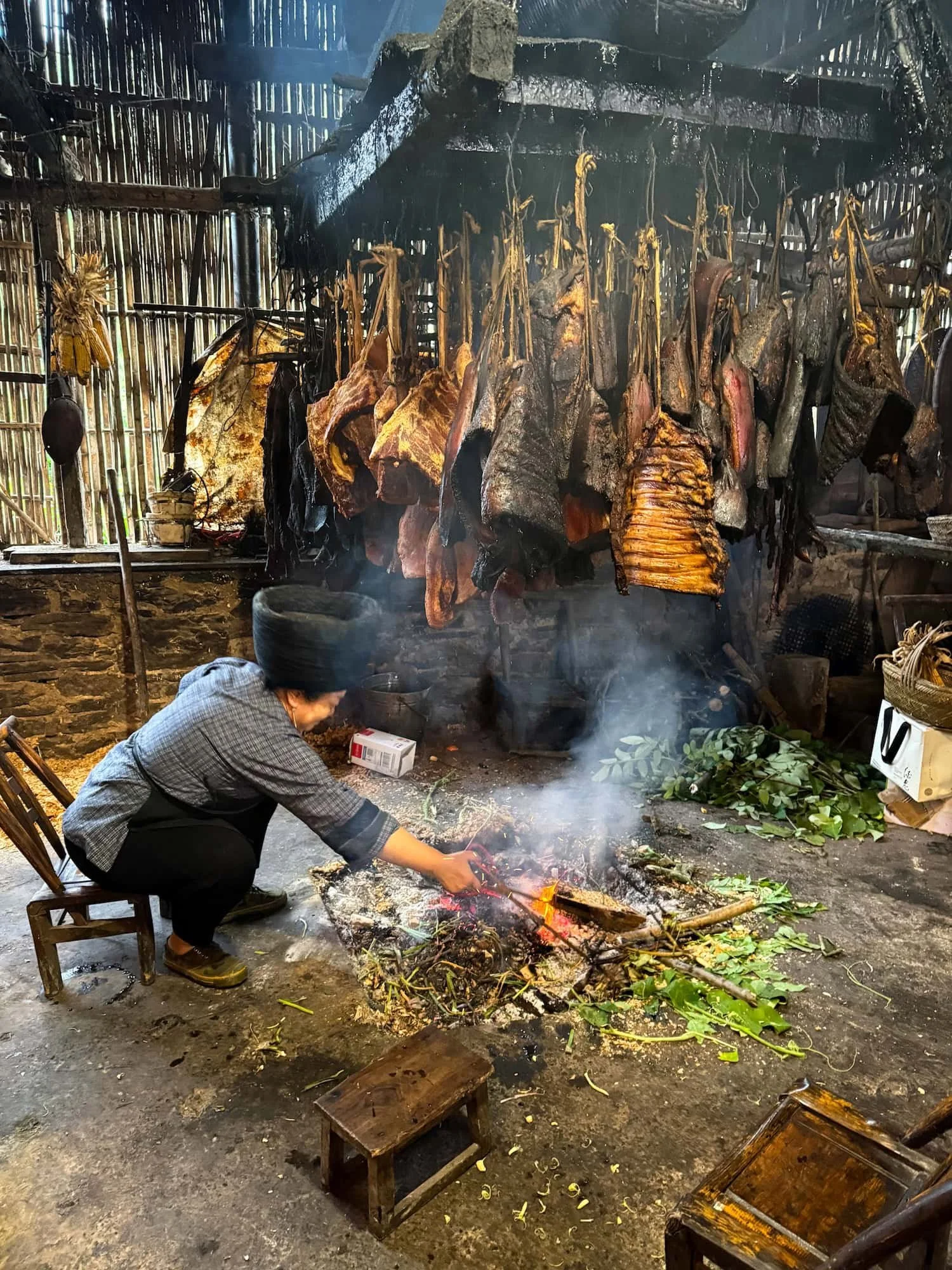 Miao villager preparing traditional smoked meat over an open fire. This 2 week China itinerary showcases authentic local cuisine and culture.