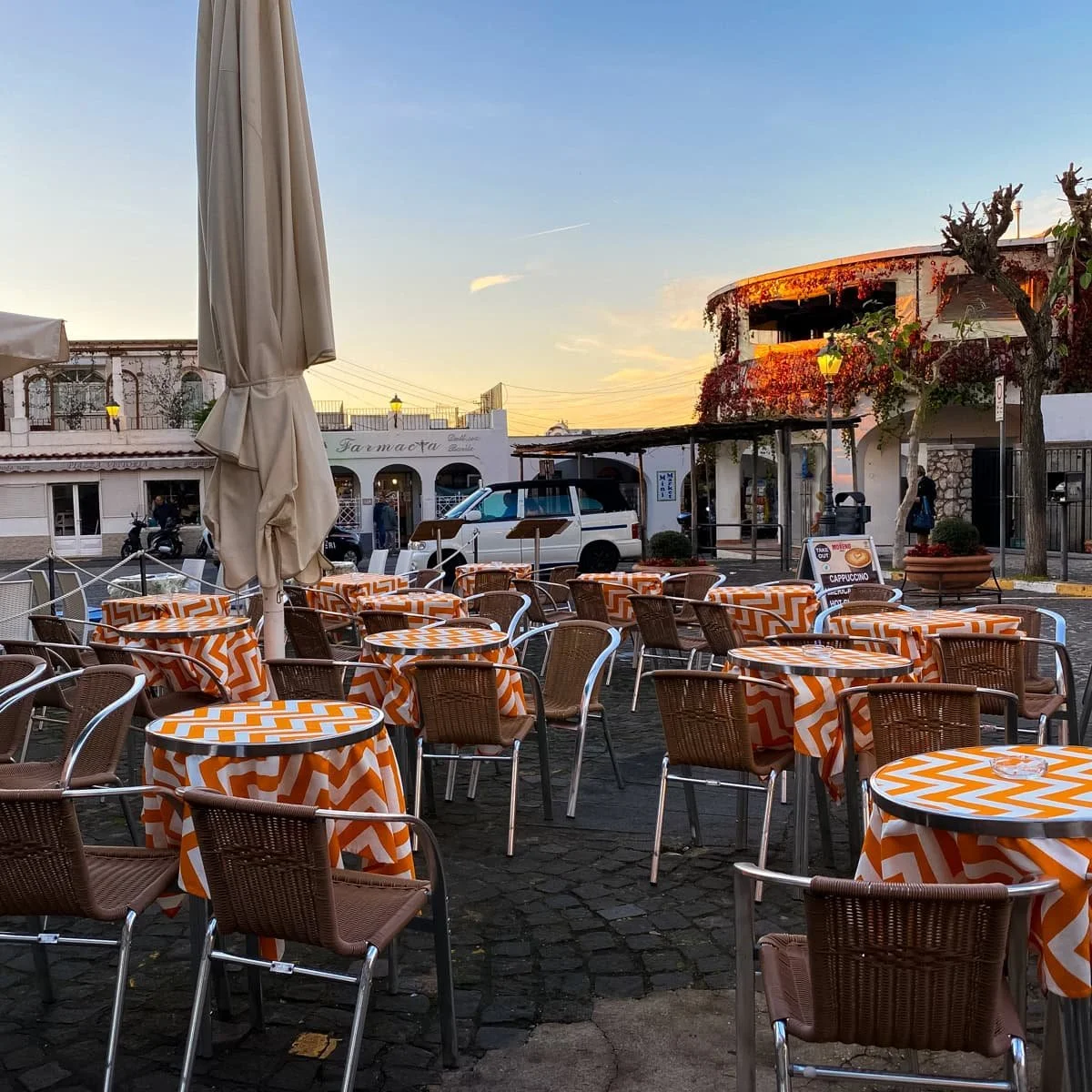 Colorful outdoor café seating with orange and white tablecloths in a charming Anacapri piazza at sunset, located near the base station of the Monte Solaro Chairlift.