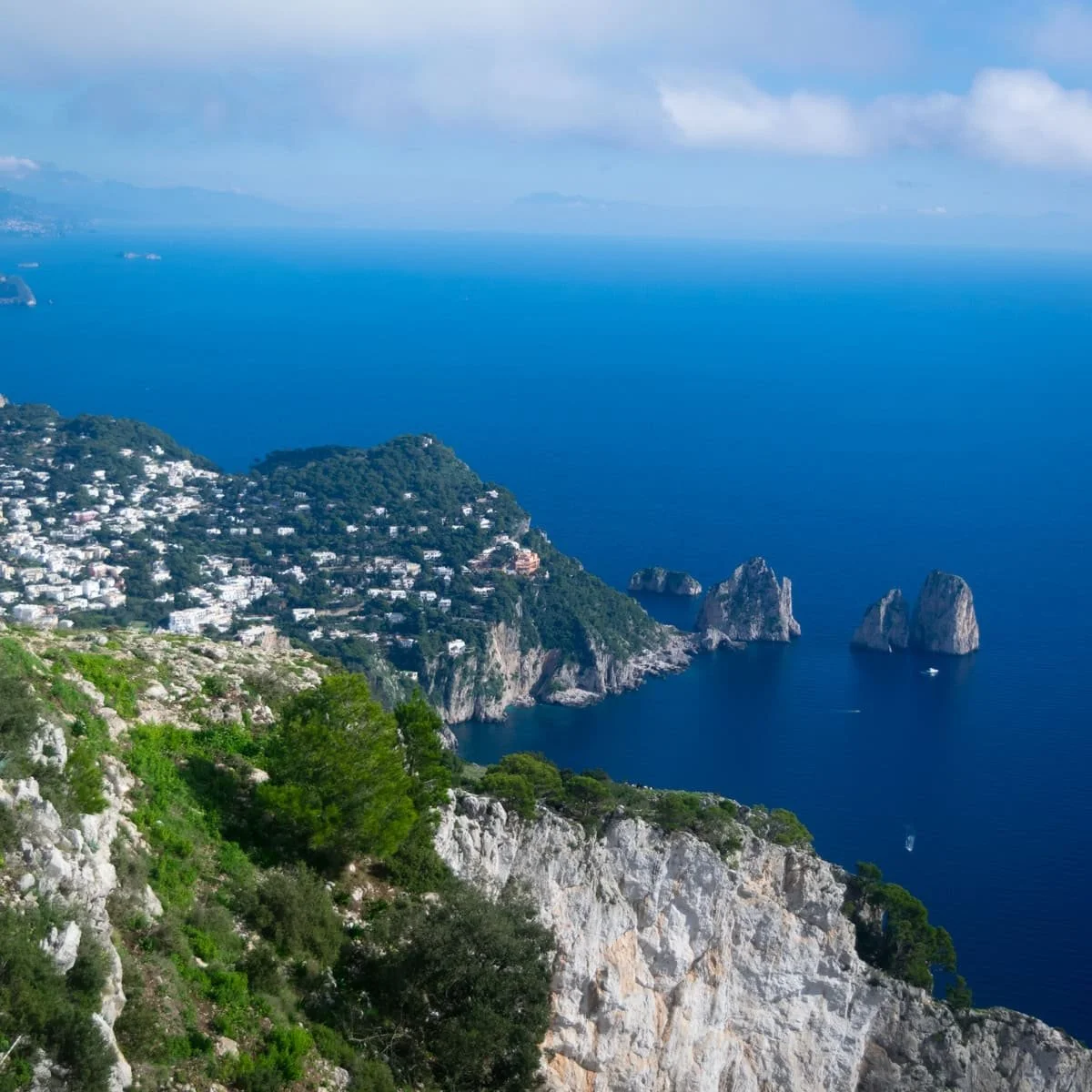 A dramatic coastal view of the Faraglioni sea stacks and Capri’s white villas from the summit of Monte Solaro, offering one of the best post-chairlift photo spots on the island.