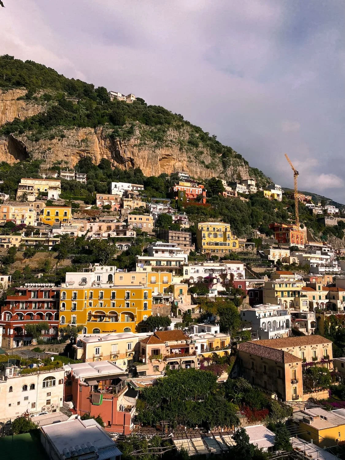 Close view of Positano’s pastel buildings stacked along steep cliffs covered in greenery. Sunlight highlights the colorful hillside homes overlooking the Mediterranean Sea.