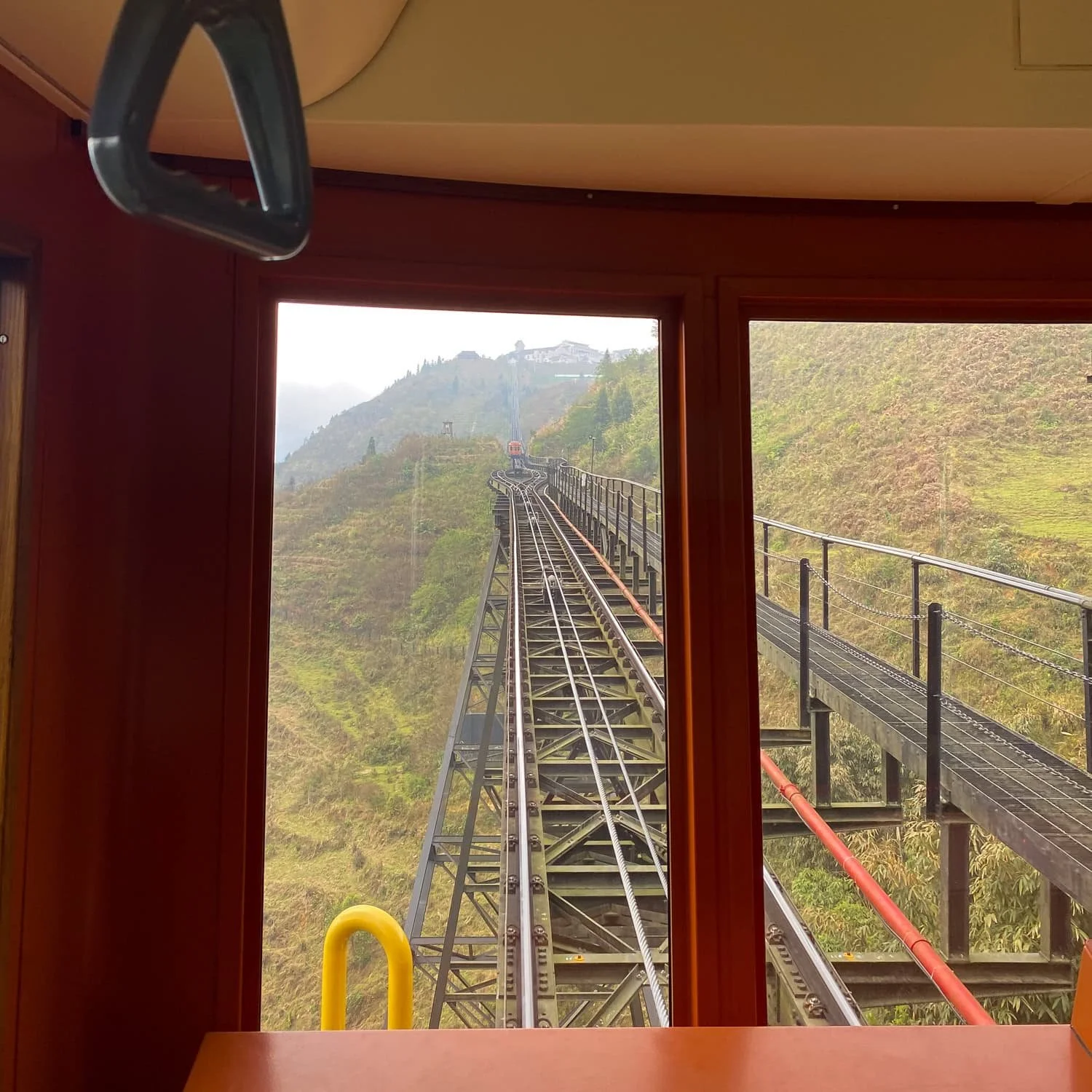 View from inside a funicular train ascending a steep track lined with metal rails and walkways in the Fansipan area.