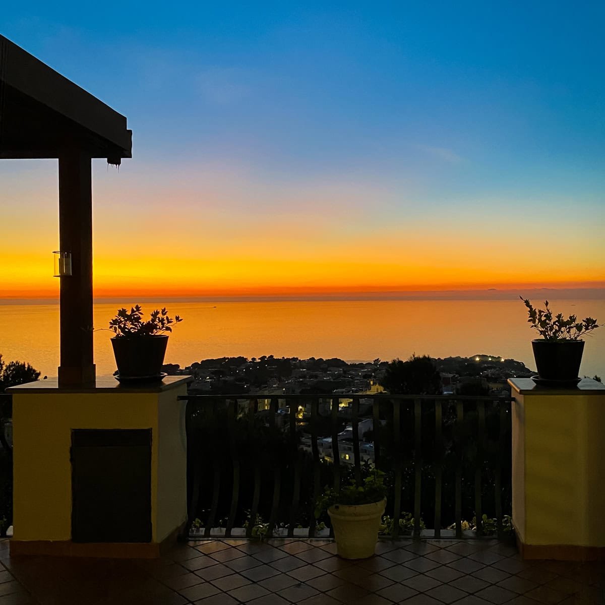 Banner image showing a stunning coastal view from a terrace at sunset, with deep orange and blue hues blending over the sea. Perfect for a blog post comparing where to stay in Capri versus Anacapri.