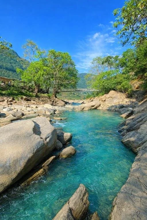 Blue-green river with rocks on all sides and trees in the distance in Sapa.