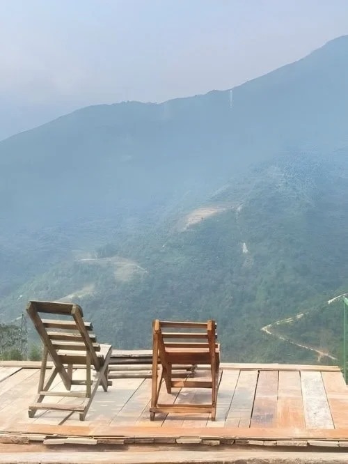 My's Homestay Sapa Exterior - two wooden chairs on a wooden platform looking out into the sapa mountains.