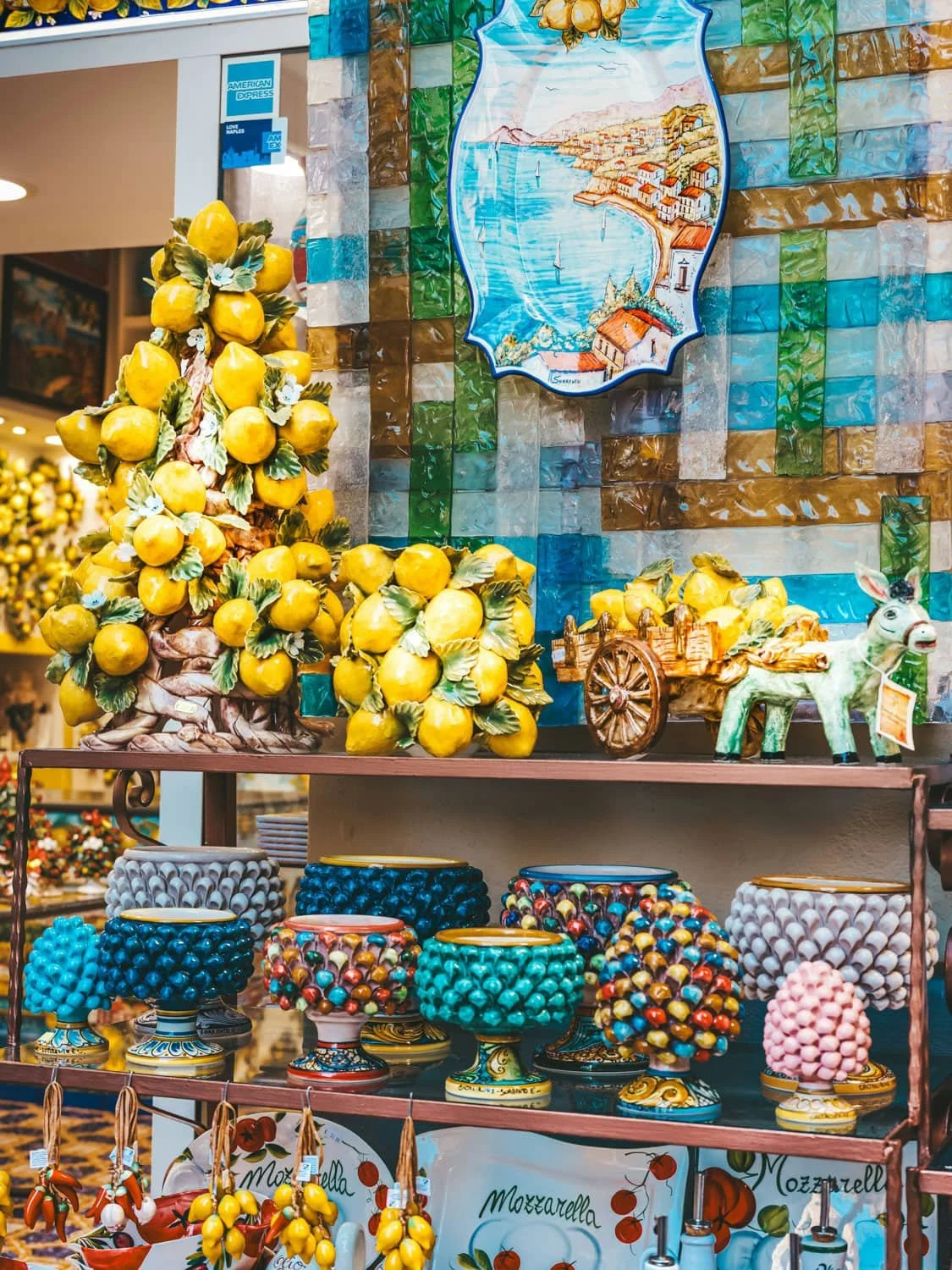 Display of colorful ceramic souvenirs and lemon themed decorations in a Positano shop. Hand painted bowls, candle holders, and pottery capture the bright coastal style of the Amalfi Coast.