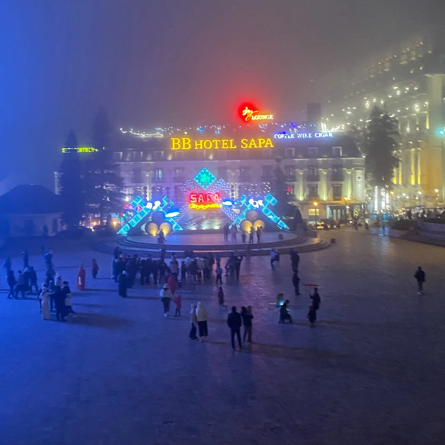 Nighttime view of Sapa's main square with neon-lit "Sapa Moments" sign in front of the BB Hotel Sapa. The poverty demonstrated by children dancing to music and selling trinkets is one of the reasons why you might want to skip Sapa.
