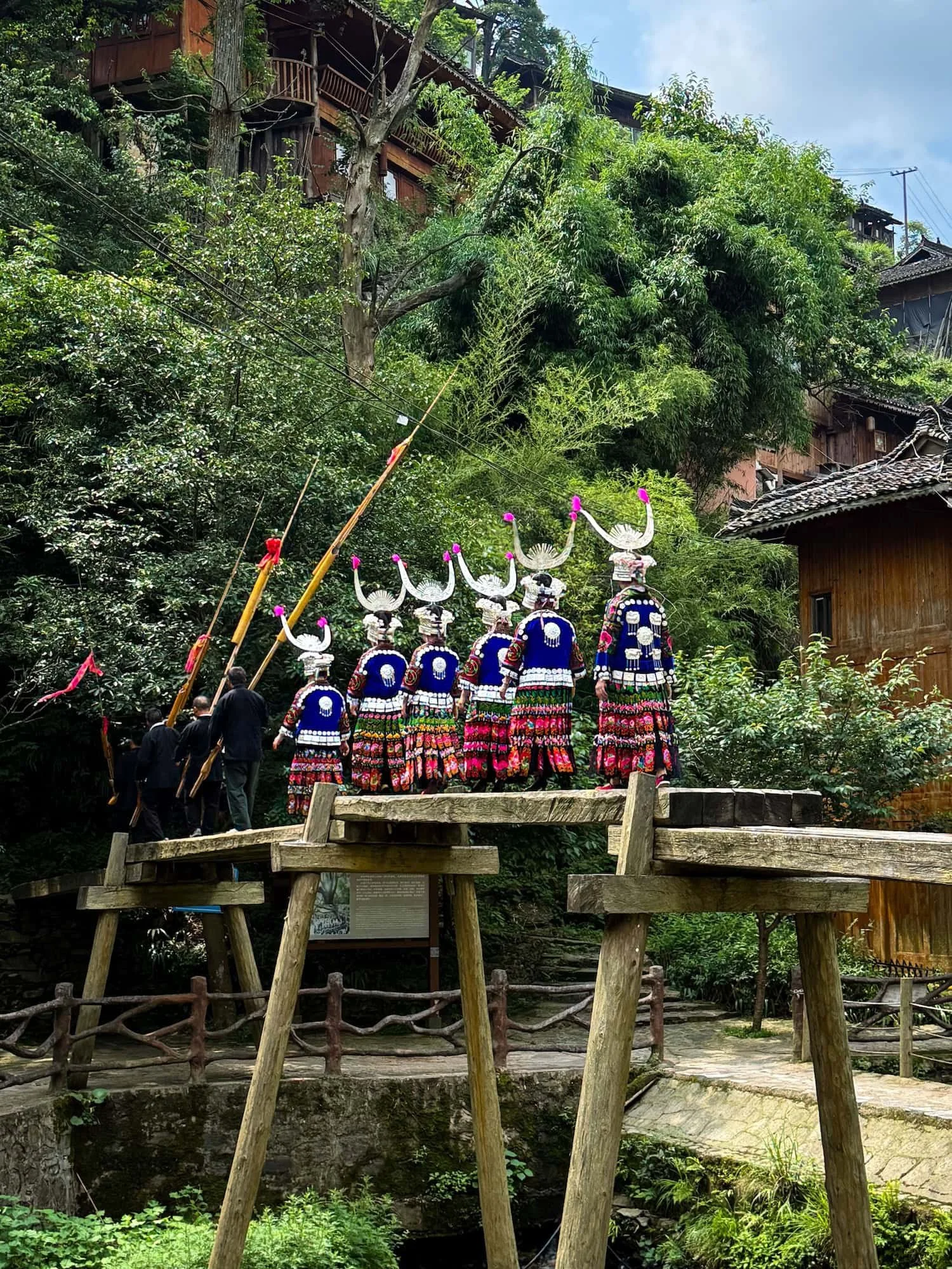 Miao villagers in traditional dress crossing a wooden bridge in Guizhou. This 2 week China itinerary showcases China's diverse ethnic cultures.