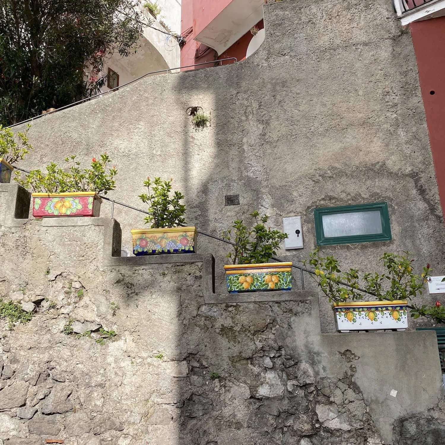 Stone staircase lined with colorful ceramic planters filled with greenery against textured walls. The details reflect the local character and design found throughout Amalfi towns.