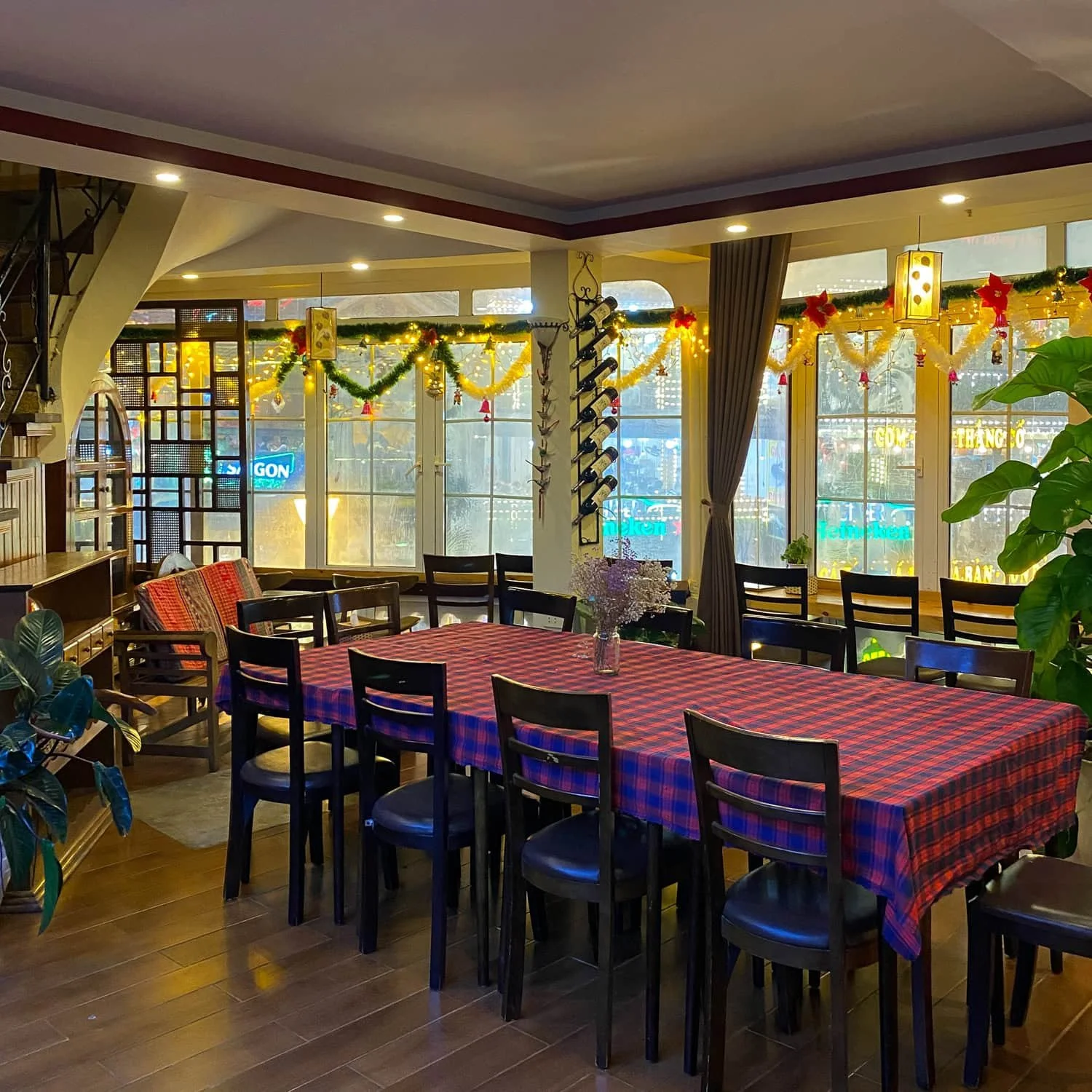 A cozy dining area with a long table covered in a red and blue checkered cloth, decorated with Christmas garlands and warm lighting, likely near the Fansipan cable car area in northern Vietnam.