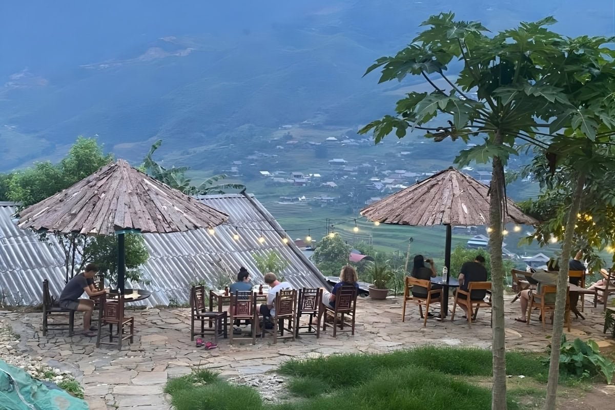 People enjoying their time outdoors at Hmong Sister House & Trekking. Wooden chairs and gtables lined along the patio overlooking the terraced rice fields of Sapa.