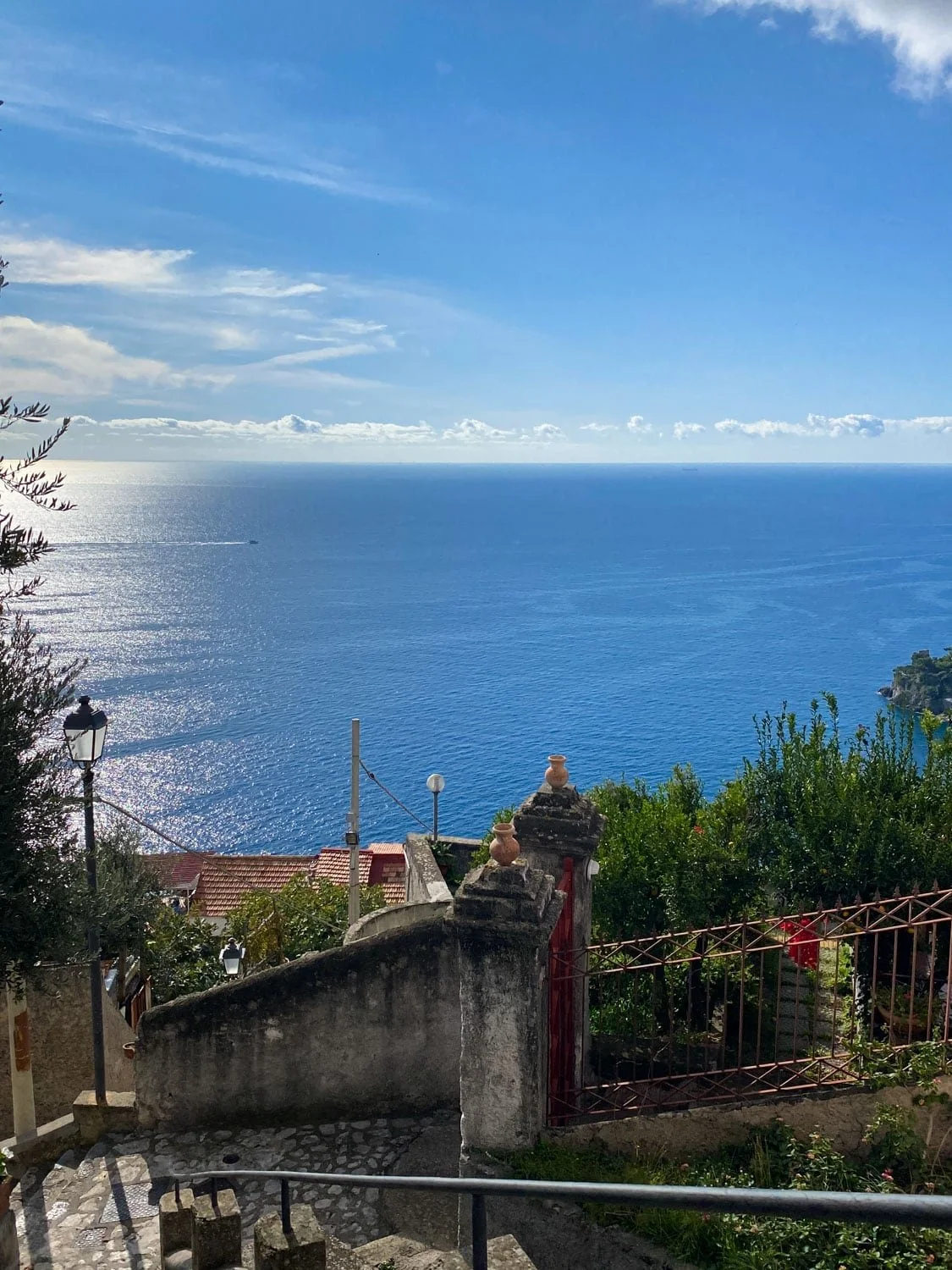 Stone stairway and wrought iron gate overlooking the sparkling blue Mediterranean Sea in Ravello. Coastal rooftops and lush greenery frame one of the most scenic things to do in Ravello.