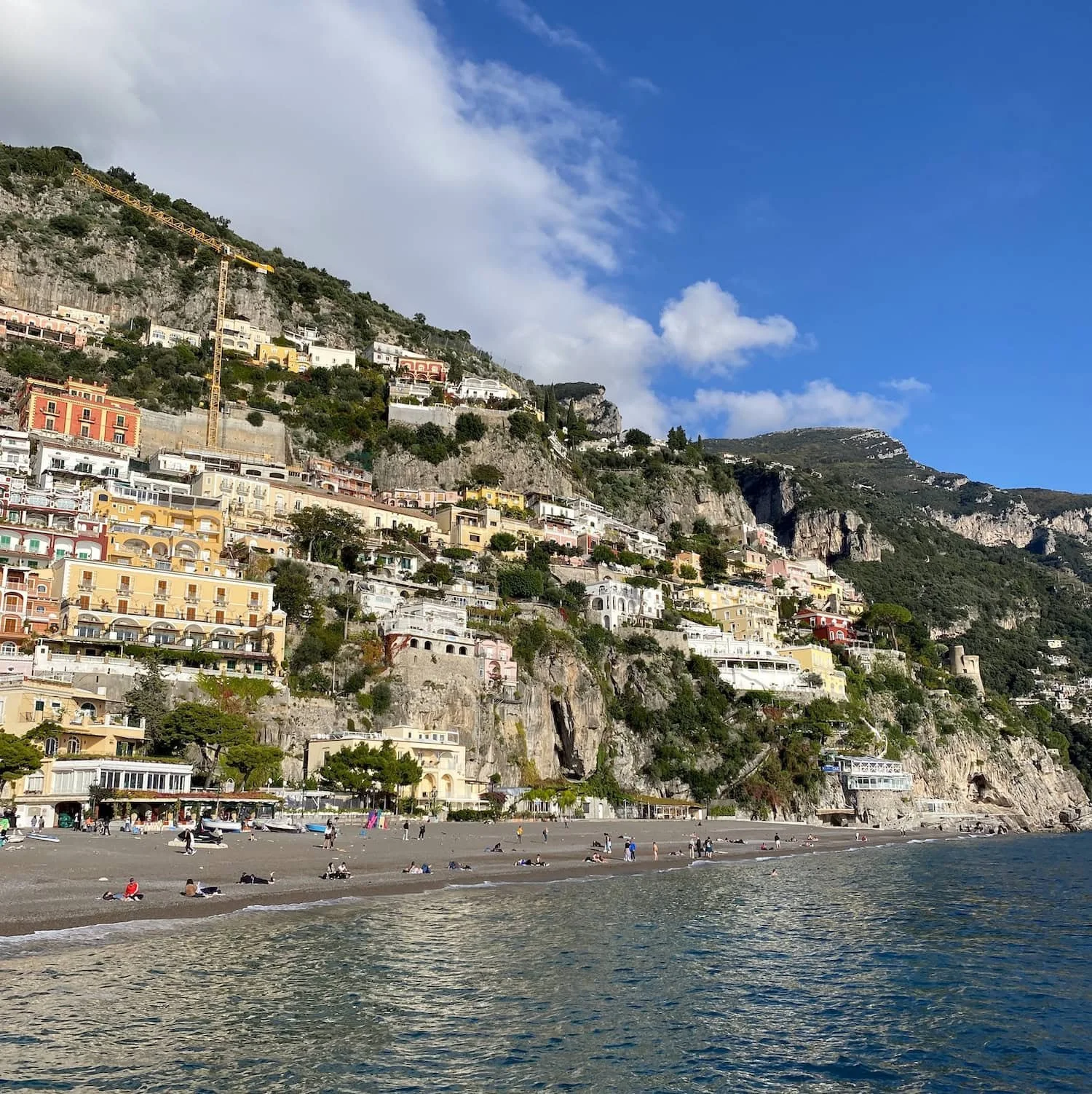 People relaxing on the beach with colorful houses climbing the steep cliffs of Positano above the shoreline. Spending time at Positano beach is one of the classic Amalfi Coast things to do.