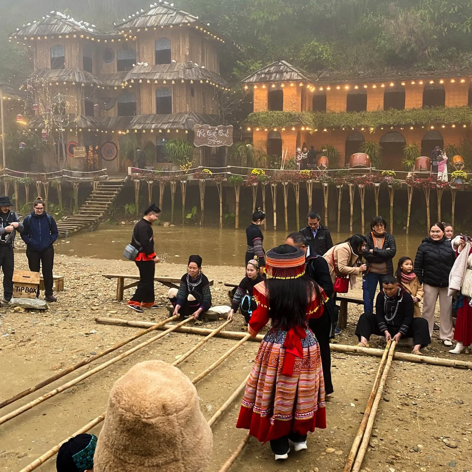A group of people, including performers in colorful traditional clothing, gather in Cat Cat Village for a cultural dance performance near the “Cat Cat Show” stage.